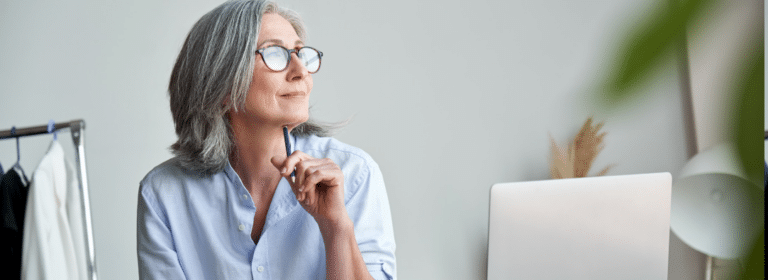 A woman looking thoughtful. She has shoulder-length gray hair, and is wearing tortoiseshell glasses and an Oxford shirt. She pensively presses a pencil against her chin.