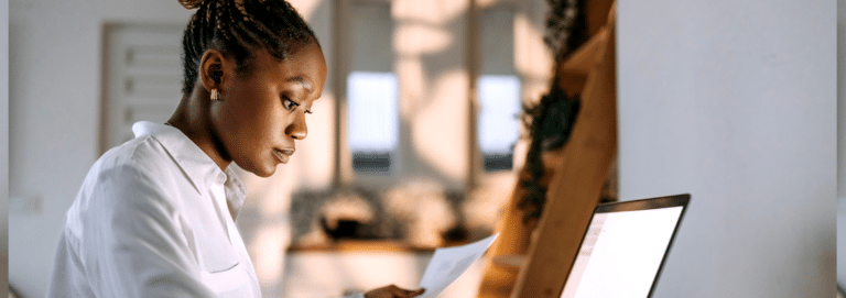 A woman looking at her laptop. Her hair is pulled back into a bun and she is wearing a white button-up shirt.