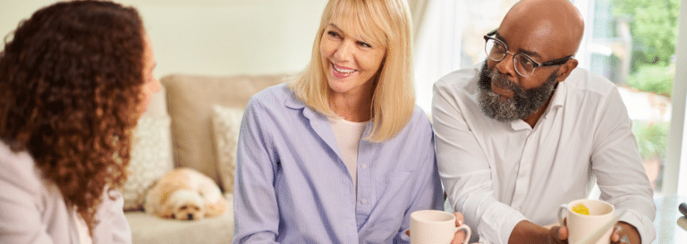 A woman in a pinstriped blue shirt and a man in a white button-up shirt are both holding mugs and conversing with a banker.