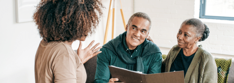 An older couple, both wearing green sweaters, are meeting with a banker.