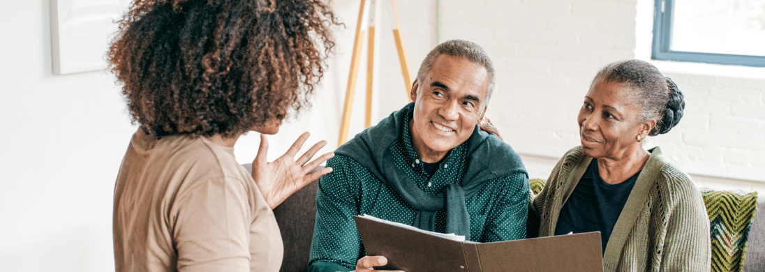 An older couple, both wearing green sweaters, are meeting with a banker.