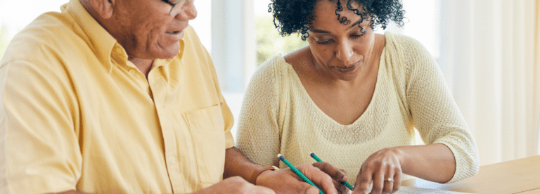 A man and a woman, both wearing yellow shirts, are signing a document together.