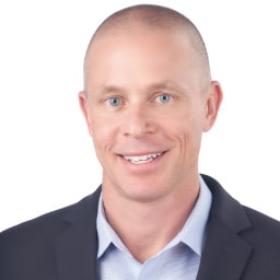 A headshot of associate Adam Rieger. He is smiling at the camera and wearing a black suit.