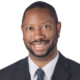 A headshot of associate Christopher Williams. He has short black hair and he is wearing a black suit.