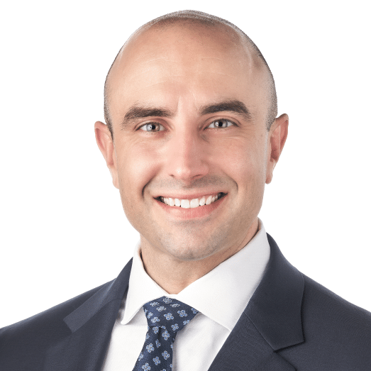 A headshot of associate Erik O'Neal. He is smiling at the camera and wearing a black suit.