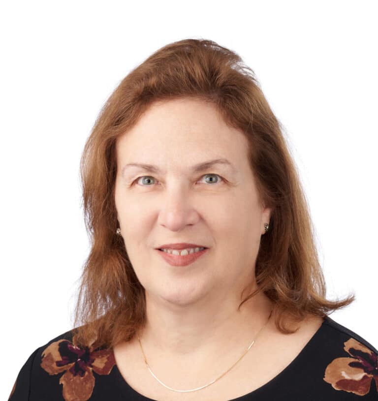 A headshot of associate Barbara Pettit. She has shoulder-length red hair, and is wearing a dress with a floral pattern.