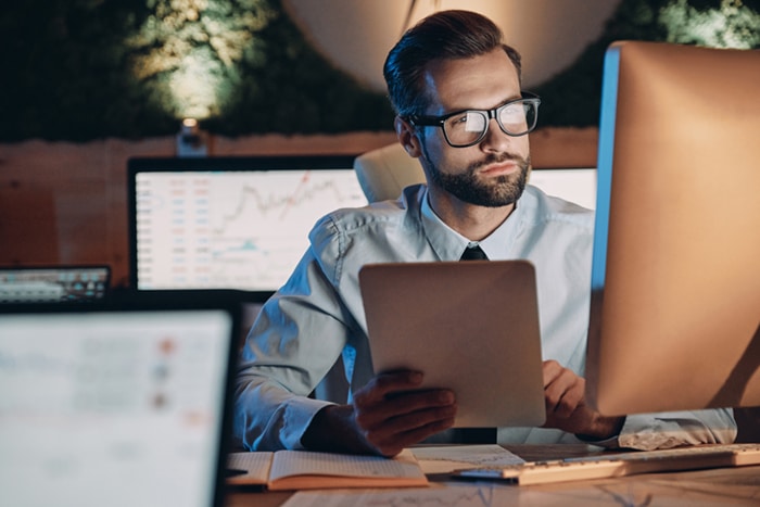 A businessman using a tablet and looking at multiple screens.