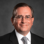 A headshot of associate Philip Wagner, CFA. He is wearing rectangular wire frame glasses and a black suit.