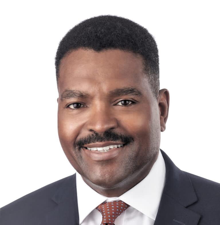 A headshot of associate Tennie James, a man with short black hair, wearing a black suit.