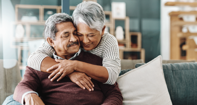 An older woman embracing her husband from behind.