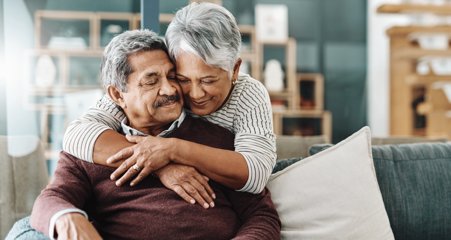 An older woman embracing her husband from behind.