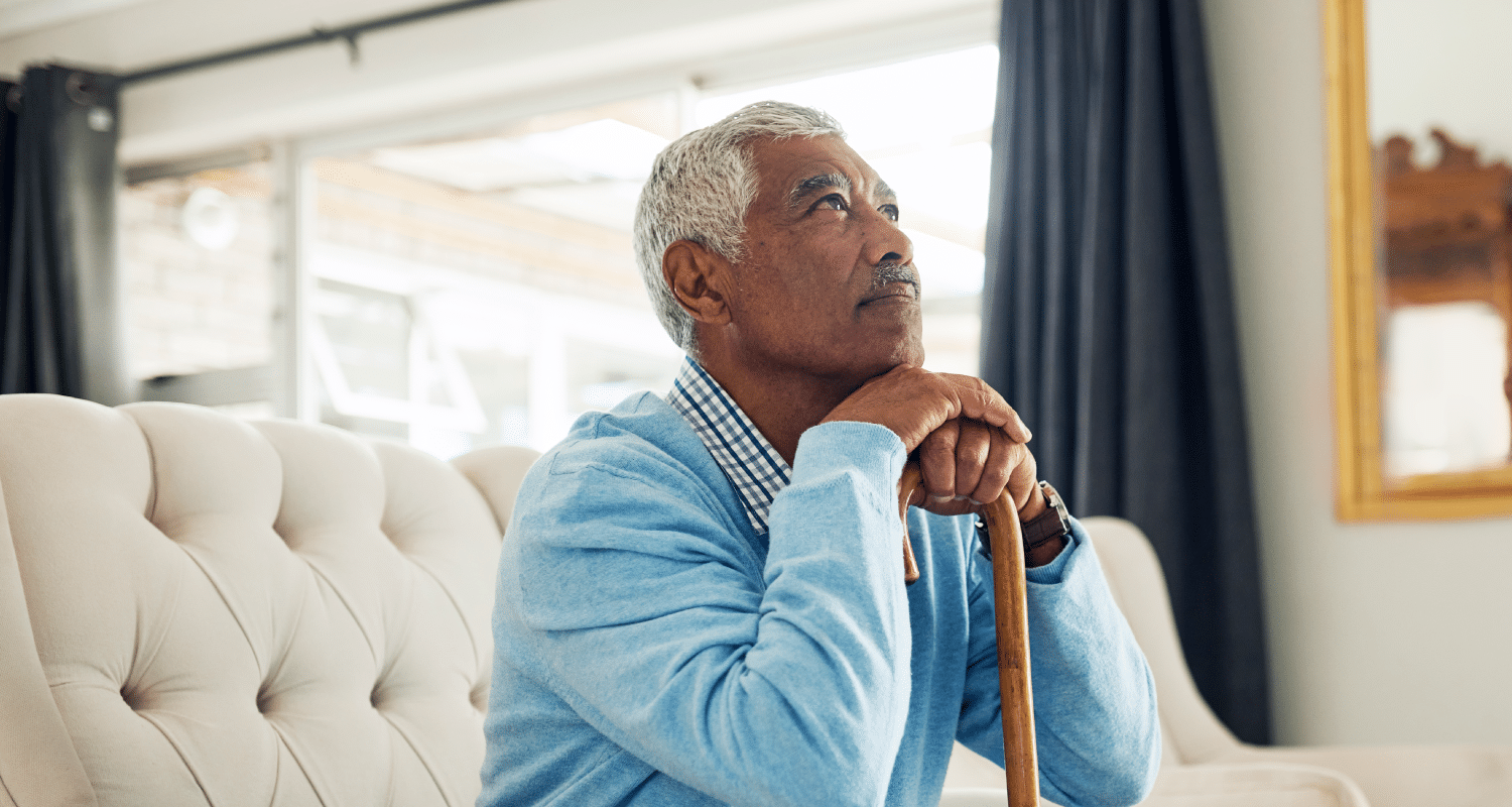 An older man, his head resting on his hands, which are folded over a wooden cane.