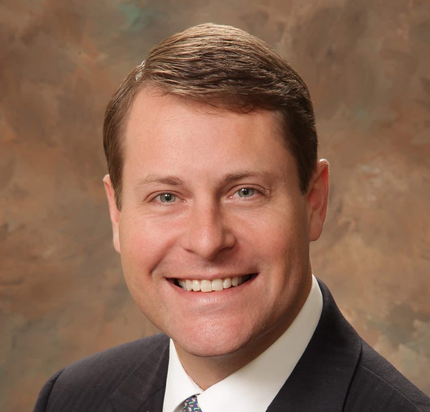 A headshot of associate Brandon Shuler. He has short brown hair and is wearing a black suit.