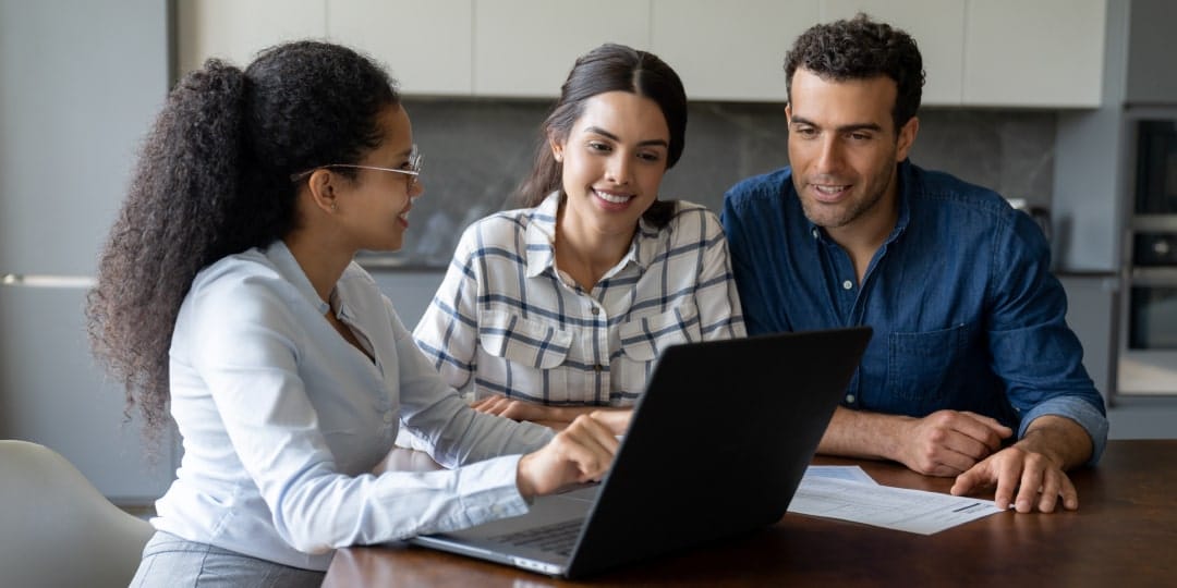 A group of people sitting around a laptop computer.